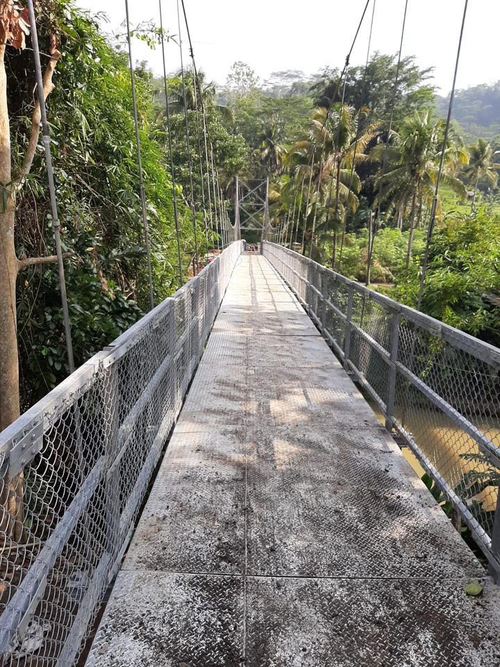 Jembatan gantung baja dengan pagar jaring di tepi sungai