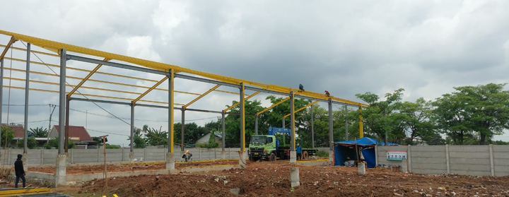 Rangka baja gudang berwarna kuning sedang dipasang di lahan proyek